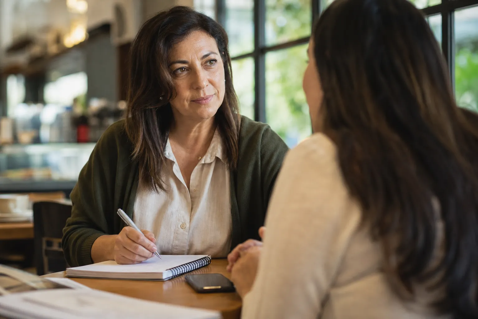 Empresária conversando com uma cliente e anotando respostas em um caderno