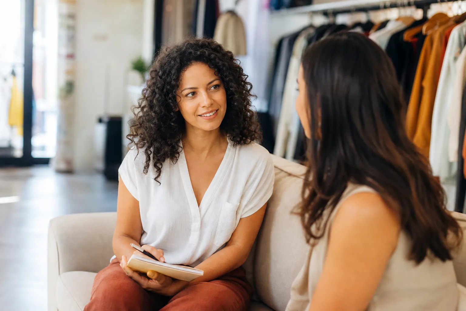Dona de loja de roupa conversando com uma cliente e anotando as respostas em um caderno